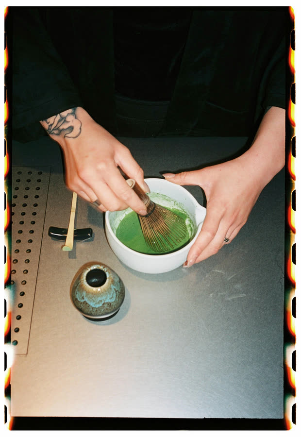 Manos batiendo un matcha en un cuenco blanco sobre la barra
